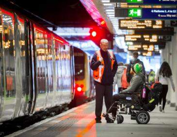 Wheelchair user in a railway station platform being assisted by a member of staff